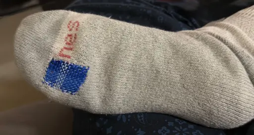 A photo of the bottom of a white and gray sock. A hole has been repaired with a woven blue patch that has several shades of blue in it 