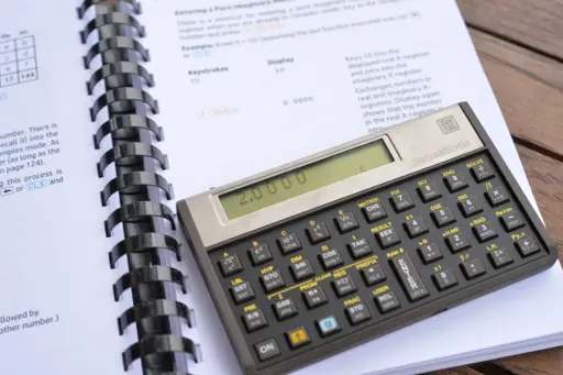 A swiss micros DM-15L sat on a printed out and ring-bound HP-15ce calculator manual.  It is displaying the number of the calculation i^(-2ln(2)i/pi)