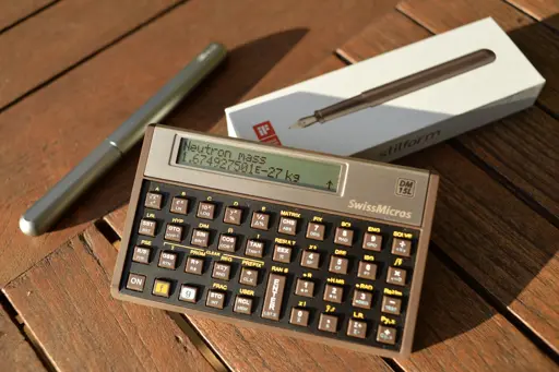 DM-15L propped up outside on a table.  It displays two lines.  Top line says Neutron mass, and below is the value.  There is a silver pen and pen box in the background.